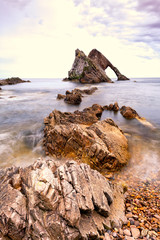 Long exposure of landmark Bow Fiddle Rock in Scotland with rocks and pebbles in foreground in warm...