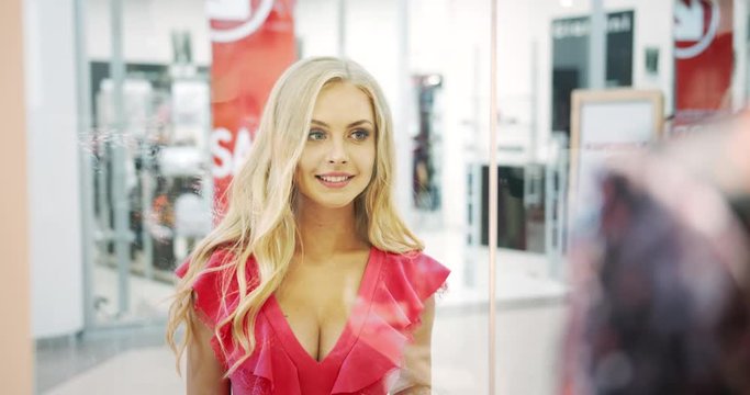 Beautiful blonde woman in feminine dress looking in shop showcase during seasonal sales, fashion industry