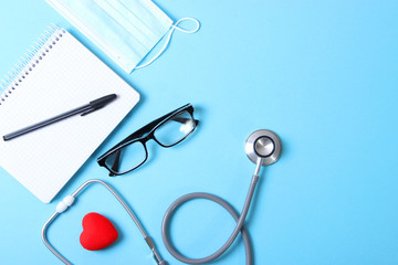 Doctor's desk top view. Stethoscope, pills, glasses and notebook on a colored background.