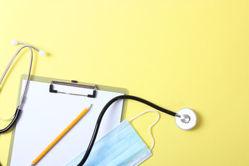 Doctor's desk top view. Stethoscope, pills, glasses and notebook on a colored background.