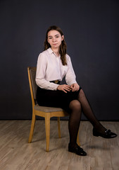 Portrait of a brunette girl with long hair sitting on a chair.  Shooting in the studio, plain background.