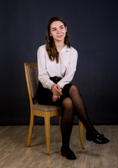 Portrait of a brunette girl with long hair sitting on a chair.  Shooting in the studio, plain background.