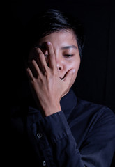 Asian men aged 21-29 years old Made his face sad and covered his eyes in the black background