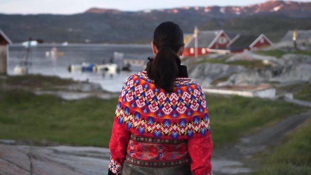 Woman in red traditional dress walking on mountain against harbor - Disko Bay, Greenland