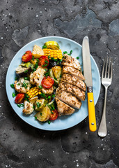 Chicken breast baked with potatoes, cauliflower, corn, eggplant, zucchini, cherry tomatoes on a dark background, top view. Healthy food diet concept