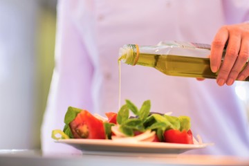 Smiling mature chef pouring oil on salad in plate at restaurant