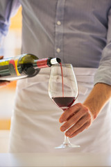 Midsection of waiter pouring red wine in wineglass at restaurant