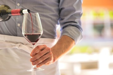 Midsection of waiter pouring red wine in wineglass at restaurant