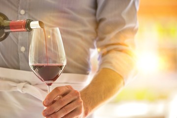 Midsection of waiter pouring red wine in wineglass at restaurant