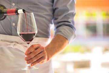 Midsection of waiter pouring red wine in wineglass at restaurant