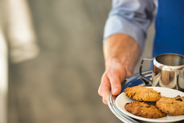 Young waiter serving coffee and cookies at restaurant