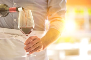 Midsection of waiter pouring red wine in wineglass at restaurant