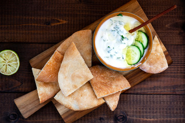 Sliced pita bread and greek yogurt with cucumber, olive oil, lemon and herbs on a wooden board. Mediterranean cuisine.