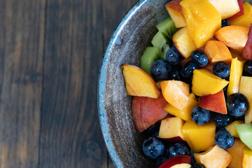 Colorful fresh fruit salad in dark bowl on wooden table in daytime