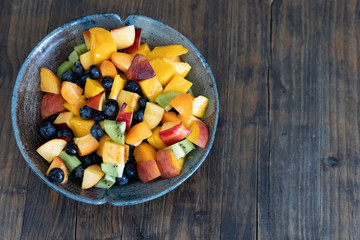 Colorful fresh fruit salad in dark bowl on wooden table in daytime