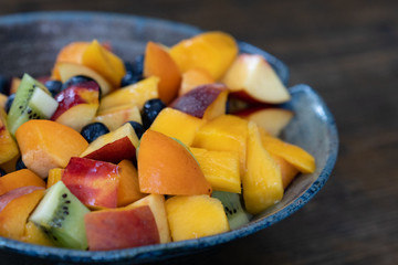 Colorful fresh fruit salad in dark bowl on wooden table in daytime