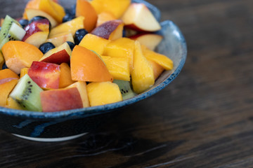 Colorful fresh fruit salad in dark bowl on wooden table in daytime
