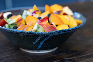 Colorful fresh fruit salad in dark bowl on wooden table in daytime