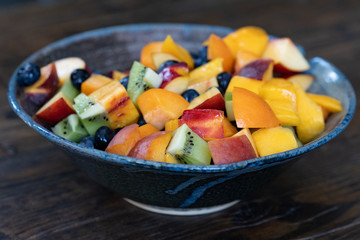 Colorful fresh fruit salad in dark bowl on wooden table in daytime