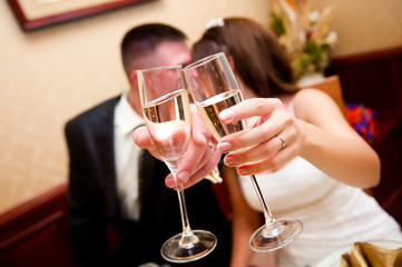 newlyweds pull glasses with champagne forward, covering their faces, kiss