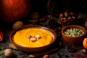 Pumpkin soup with crackers, nuts, seeds on an autumn table.