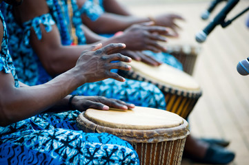 hands of African drummers in blue costumes and traditional drums in front of microphones at a...