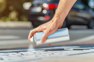 Male hand holds an aerosol can with white paint. Surface painting, graffiti on the street