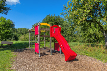 Fototapeta na wymiar Klettergerüst für Kinder mit roter Rutsche in einem Park im Sommer