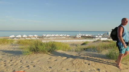 A man with a barefoot backpack is walking barefoot along the beach against the background of the sea.