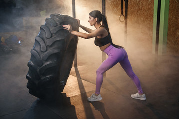 Obraz na płótnie Canvas Fitness woman flipping wheel tire in gym.