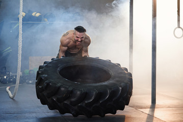 Young strong man flipping tire in the gym.