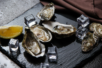 Opened oysters, ice and lemon on stone table. Served table in restaurant with fresh oysters shells...