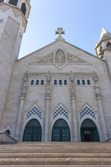 Big white cathedral with cross and three doors and stairs. Catholic church with open door. Religion and faith concept. Entrance to the beautiful white cathedral in Europe. Religious tourism concept. 