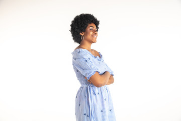 Beautiful female half-length portrait on white studio background. Young emotional african-american woman in blue dress. Facial expression, human emotions concept. Standing with hands crossed
