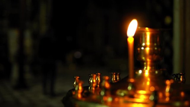 Person is baptized and bows in a Church, then camera focuses on a burning candle close up in an the Orthodox Church.