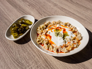 Turkish Manti with green hot pickled peppers, tomato sauce, yogurt and mint. Plate of traditional Turkish food. Top view