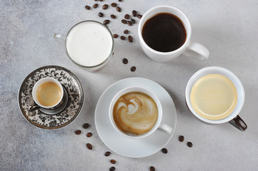 Set of different types of coffee in different cups. Espresso, cappuccino, Americano, latte are presented. Coffee beans on the surface of a light table. View from above.