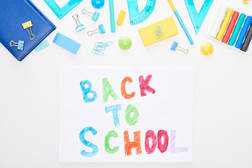 Top view of paper with back to school text near school supplies isolated on white