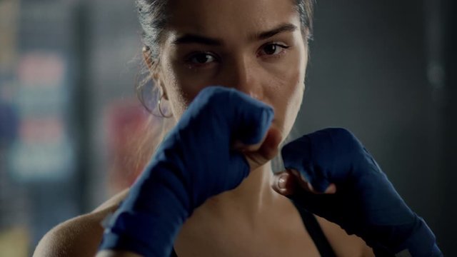 Portrait of a Beautiful Fit Brunette Kickboxer Posing Before the Camera with Her Hands Wrapped in Blue Handwraps. Her Brown Eyes Reflect Confidence and Determination. She's in an Underground Gym.