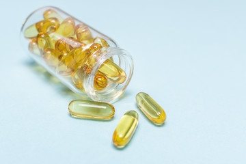 Big golden gel capsules of cod liver oil in a glass jar on blue background macro view. Omega 3 capsules close up.