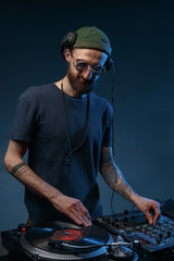 Club DJ playing mixing music on vinyl turntable at party wearing sunglasses with lens flare from nightlife lights. Creative color.