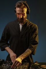 Club DJ playing mixing music on vinyl turntable at party wearing sunglasses with lens flare from nightlife lights. Creative color.