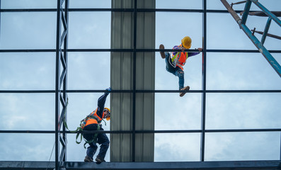 Roofer worker in protective uniform wear and gloves, using air or pneumatic nail gun and installing asphalt shingle on top of the new roof,Concept of residential building under construction.