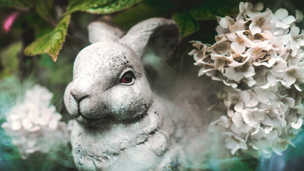 Stone rabbit hide in a bouquet of white viburnum in the garden / forest. Smoke / foggy atmosphere in the outdoor.