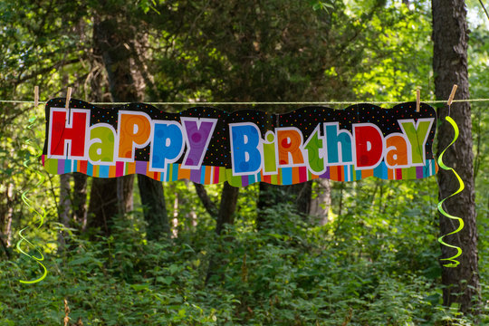Happy Birthday sign panorama in the outdoor trees with balloons and ribbons to celebrate and party for a child's birthday.