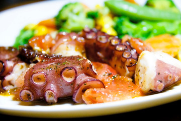 Cooked octopus with vegetables on a plate. Ready to eat sea food meal. Healthy eating concept.