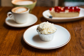 muffin with Piece of homemade strawberry cake and two cups of cappuccino with latte art on wooden background. Small and big ceramic cups.