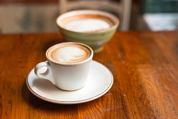 Two cups of cappuccino with latte art on wooden background. Concept of easy breakfast. Small and big ceramic cups
