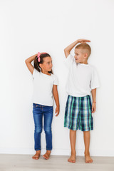Little boy and girl measuring their height isolated on white background