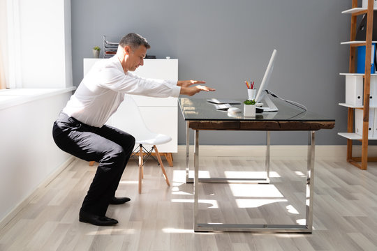 Businessman Doing Squats Exercise In Office